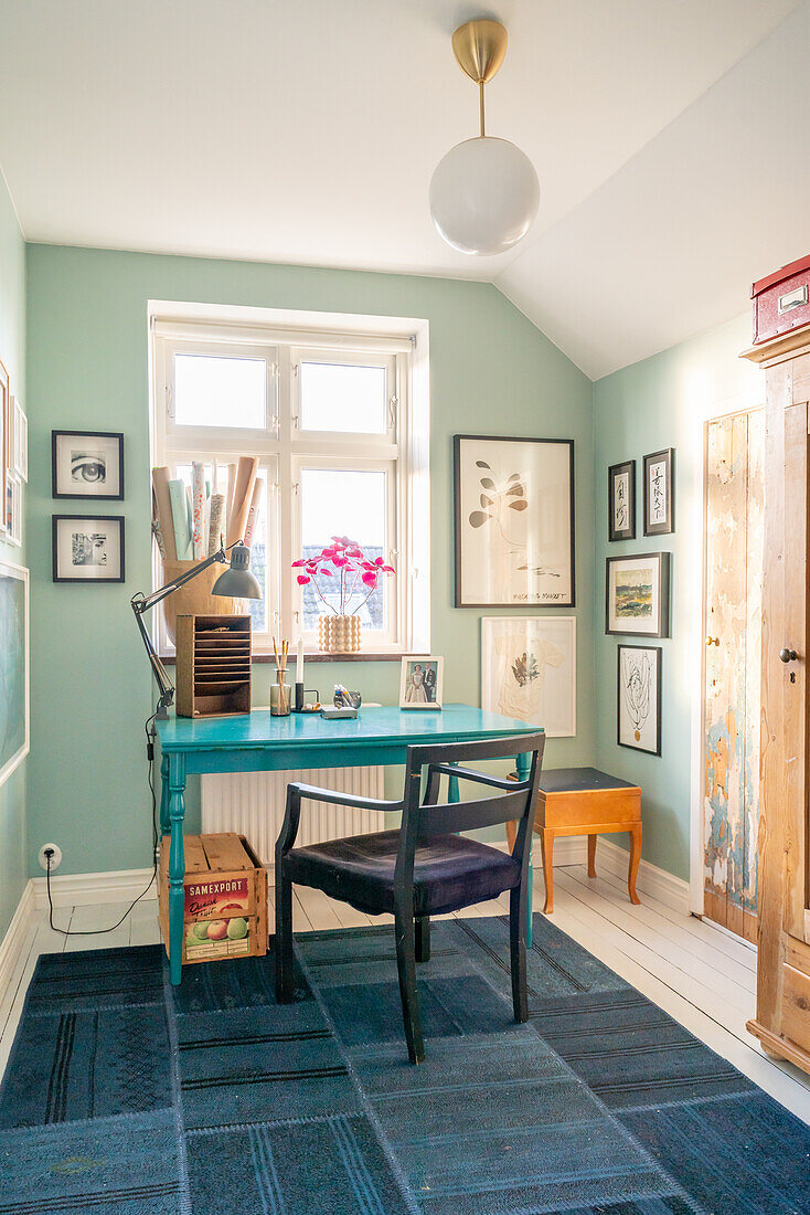 Workplace with turquoise desk and hanging lamp in a room with picture gallery