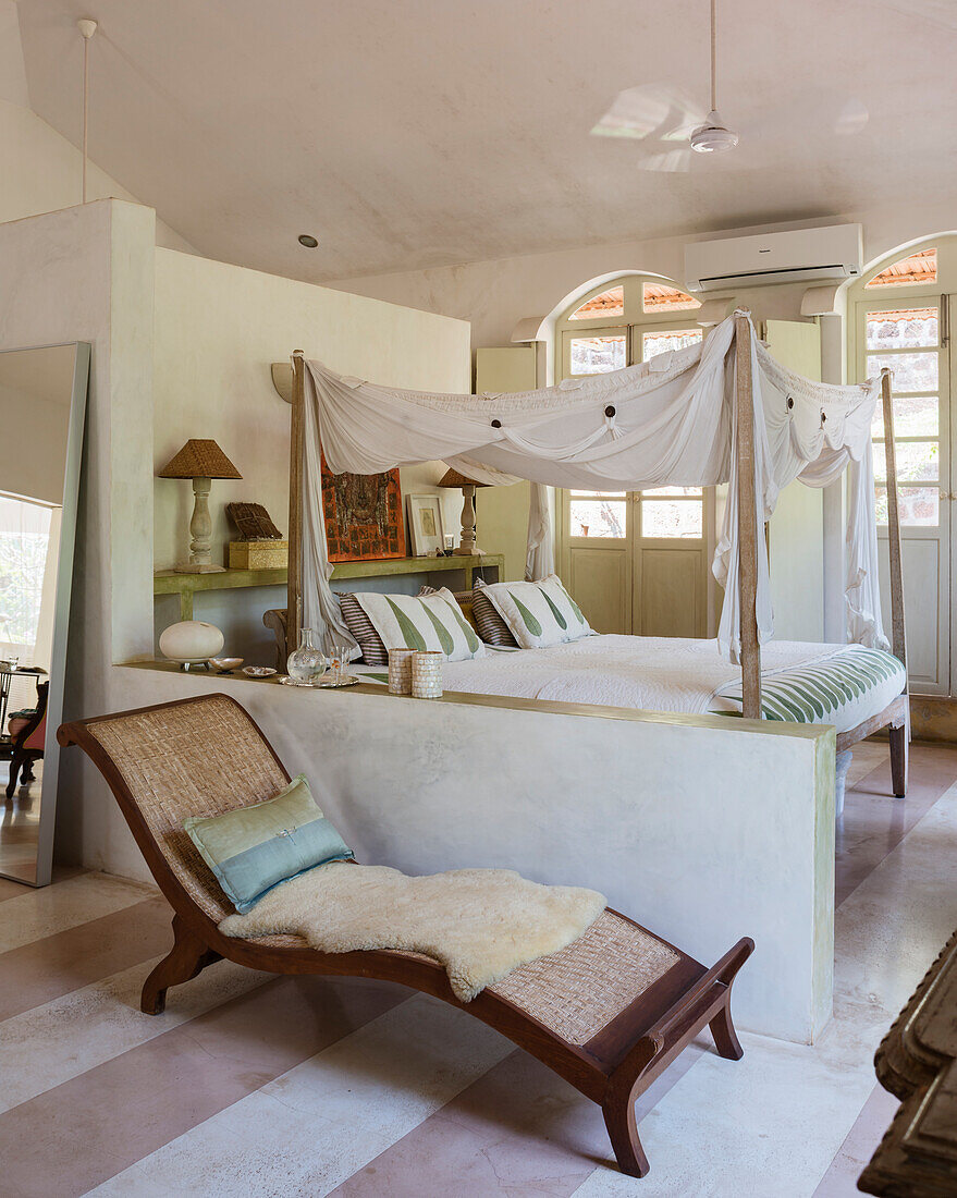 Four-poster bed with voile curtains and recliner in the bright bedroom