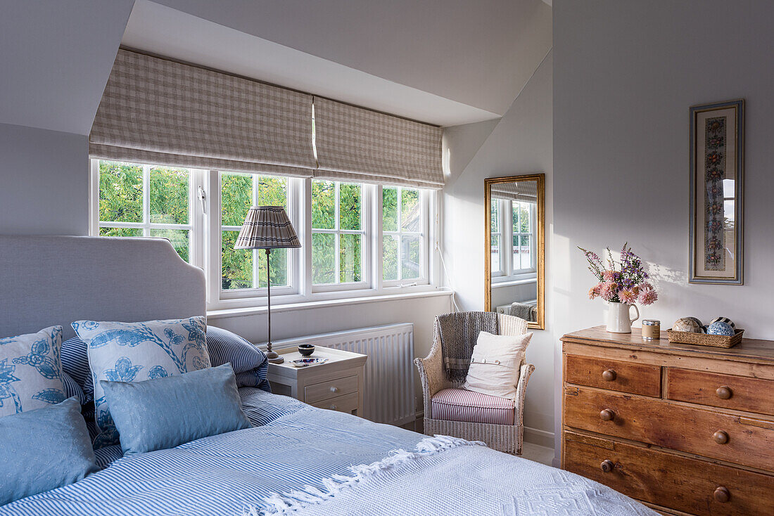 Bedroom with grey upholstered bed, light blue bed linen and wooden chest of drawers