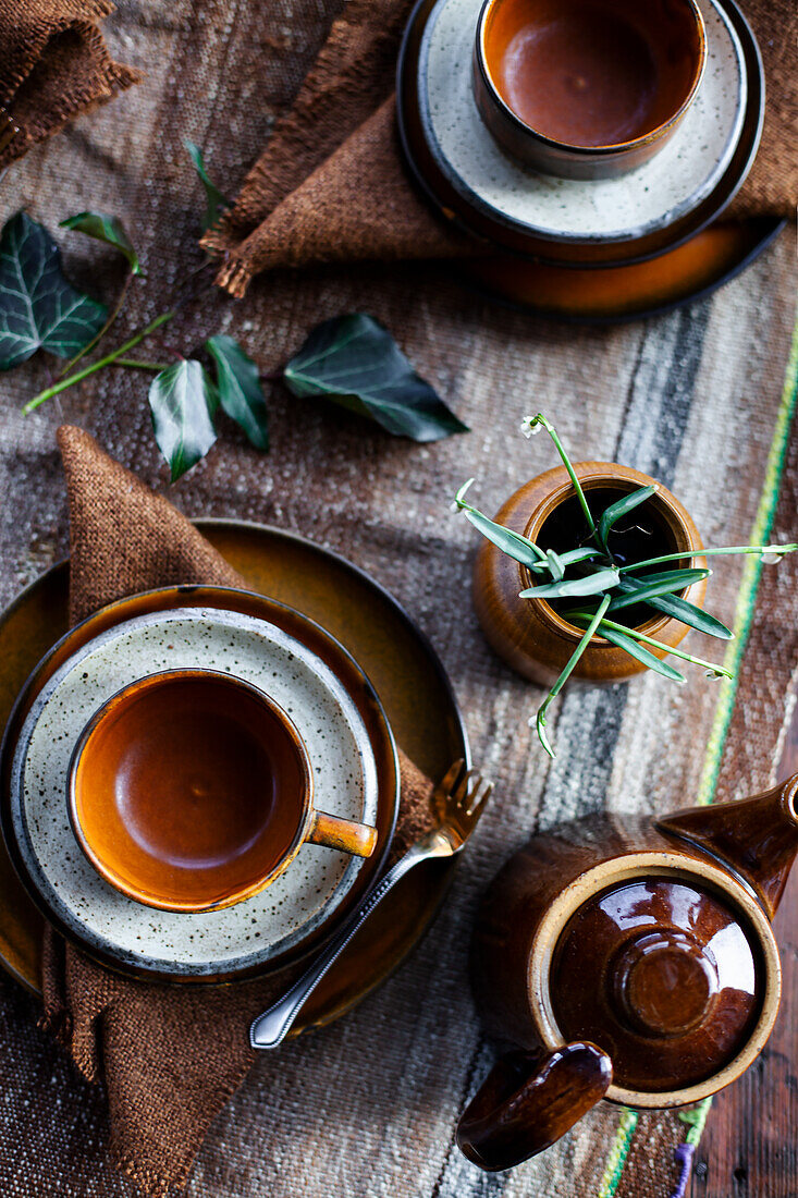 Ceramic cups and teapot on a rustic wooden table with plants and linen cloths