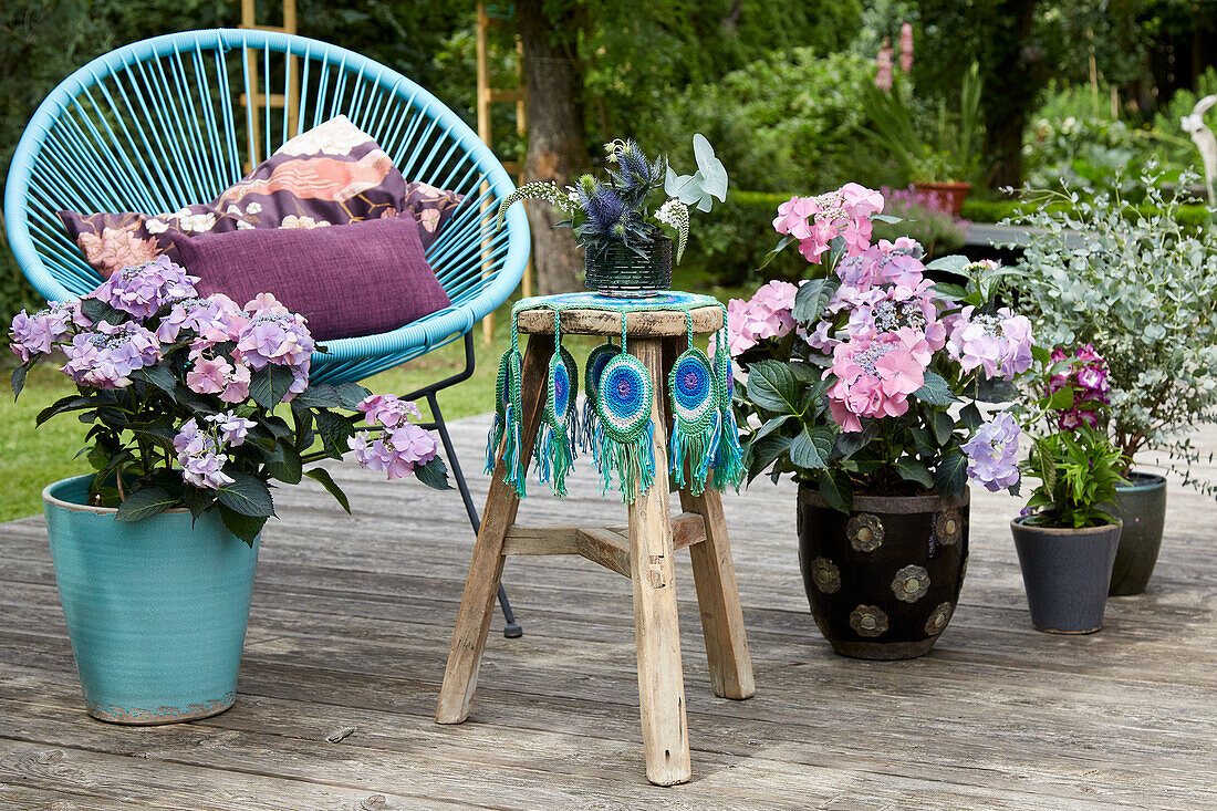 Classic chair with cushion, wooden stool with crocheted peacock feather cover and flower pots on the terrace