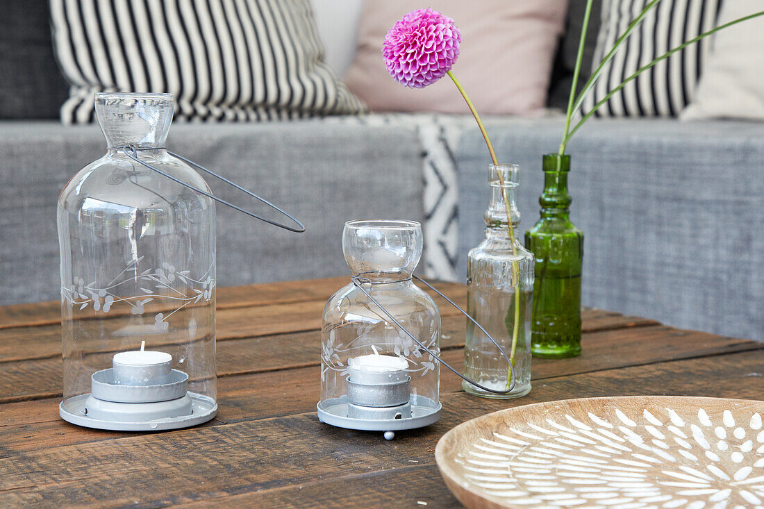 Candle lanterns and pompom dahlia in glass vase on wooden table