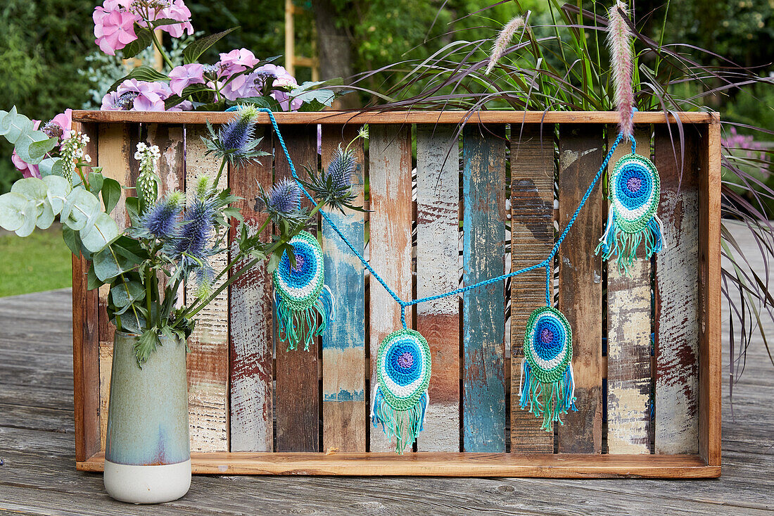 Garland with crocheted peacock feathers on a rustic wooden box