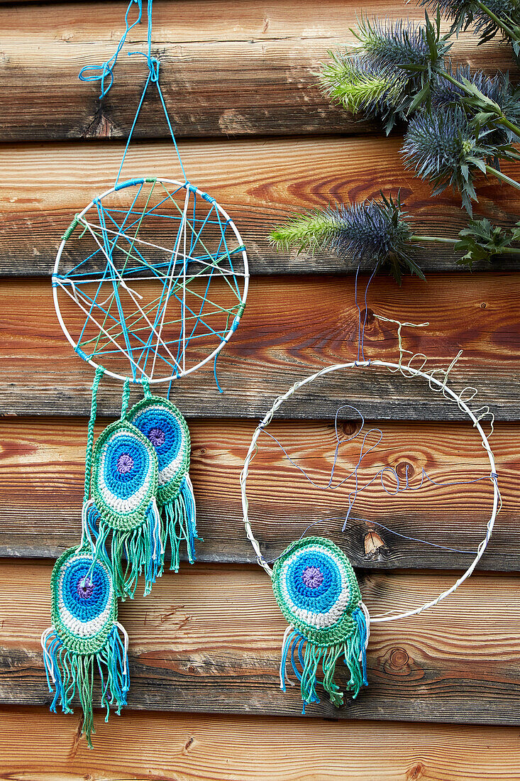 Dreamcatcher with crocheted peacock feathers in front of a rustic wooden wall