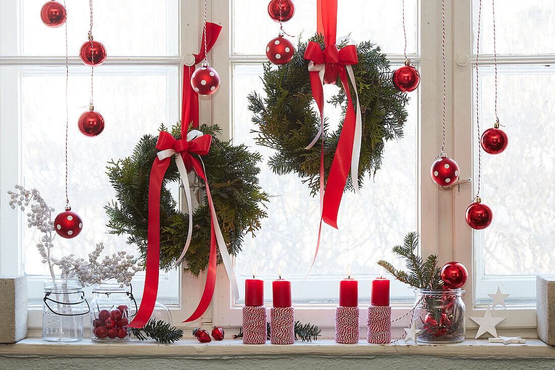 Christmas window decoration with red baubles, wreaths and candles