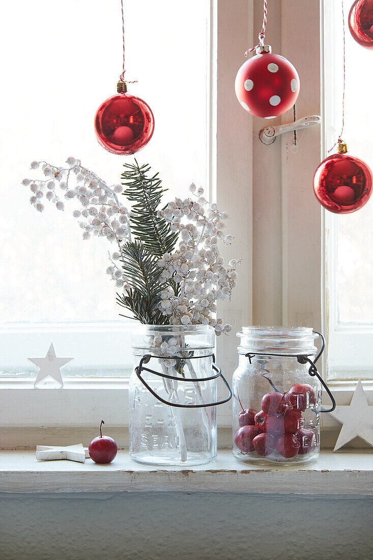 Christmas window decoration with red baubles, fir branch and storage jars