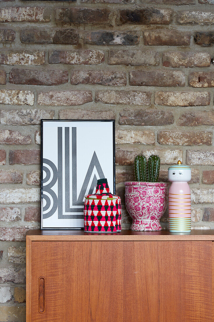 Wooden sideboard with decoration in front of brick wall