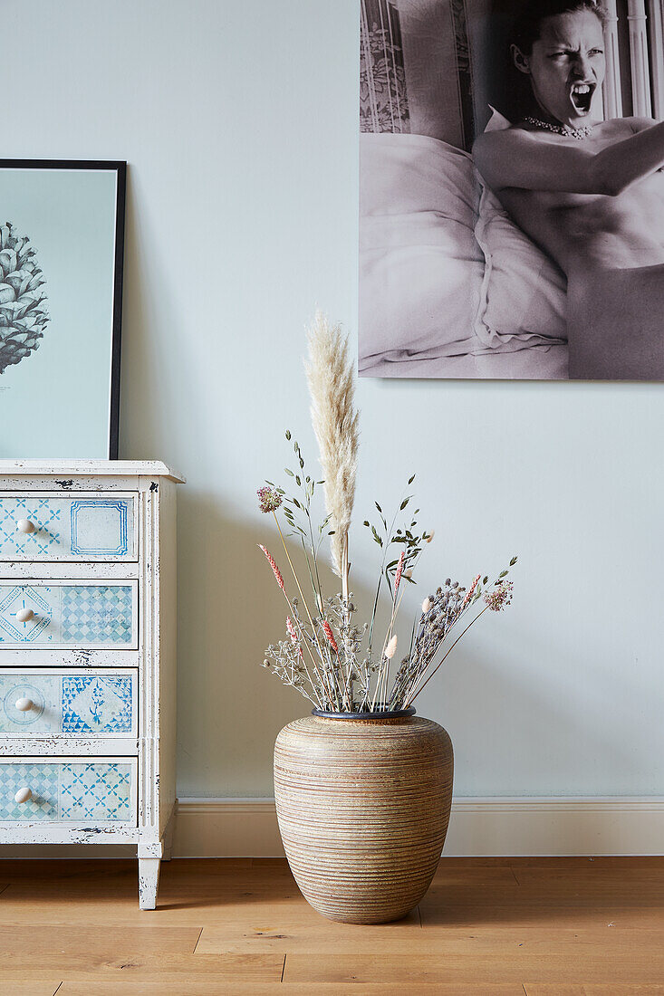 Floor vase with dried flowers next to a vintage-style chest of drawers