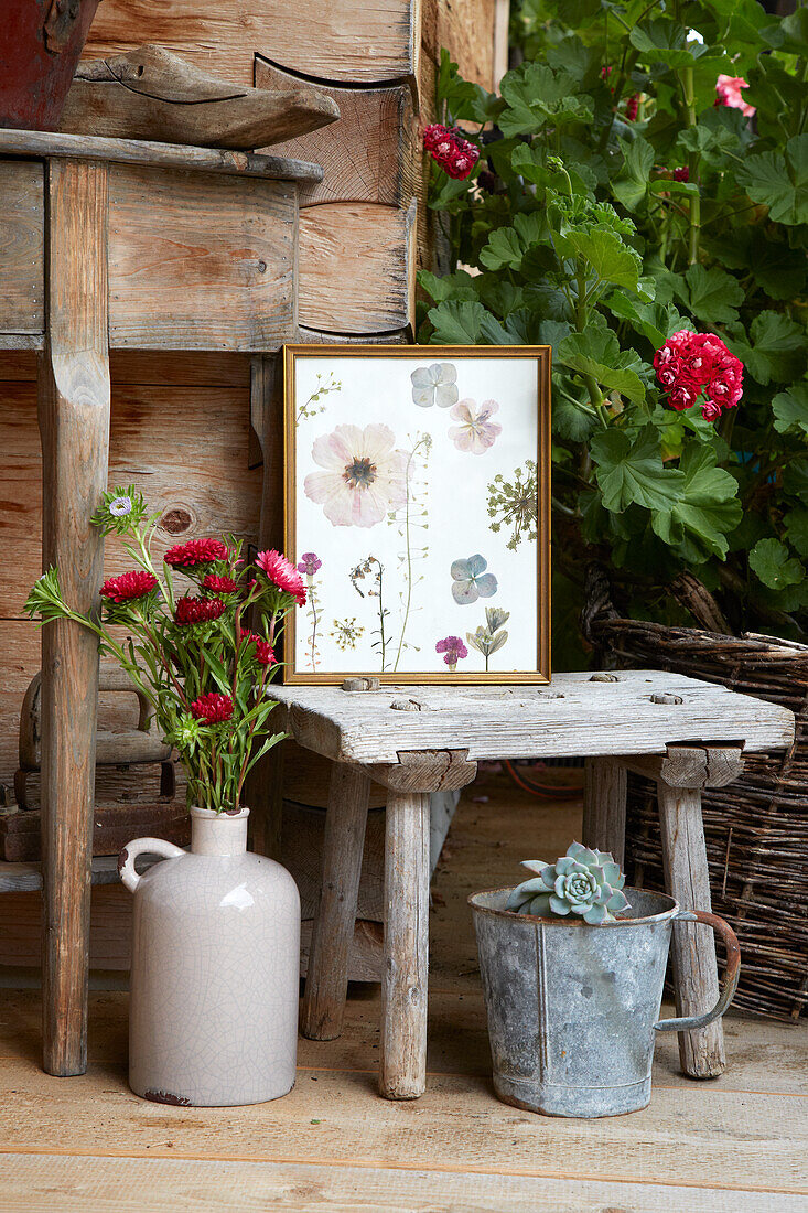 Garden decoration with vase with flowers, succulents, picture and wooden stool