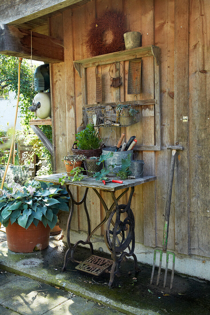 Rustic garden corner with old sewing table and tools against a wooden wall