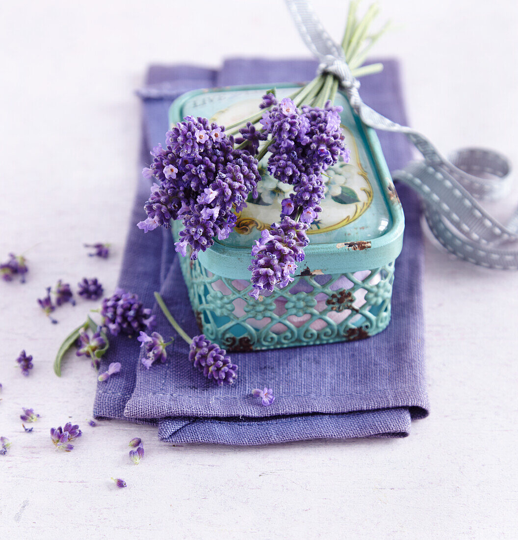 Mintfarbenes Schmuckdöschen mit Lavendelstrauß auf lilafarbenem Leinentuch