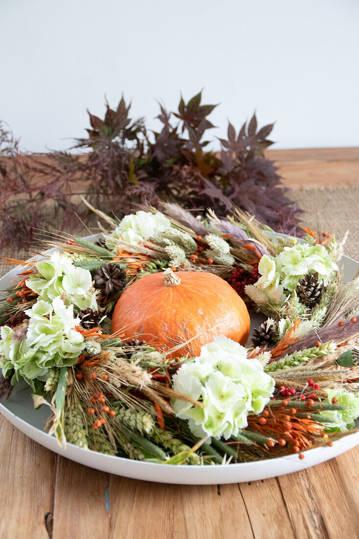 Herbstlicher Kranz mit Kürbis und Trockenblumen auf Holztisch