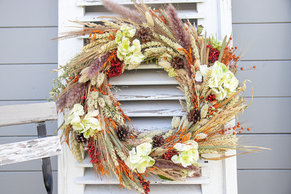 Herbstkranz aus Trockenblumen und Beeren an Vintage-Fensterladen