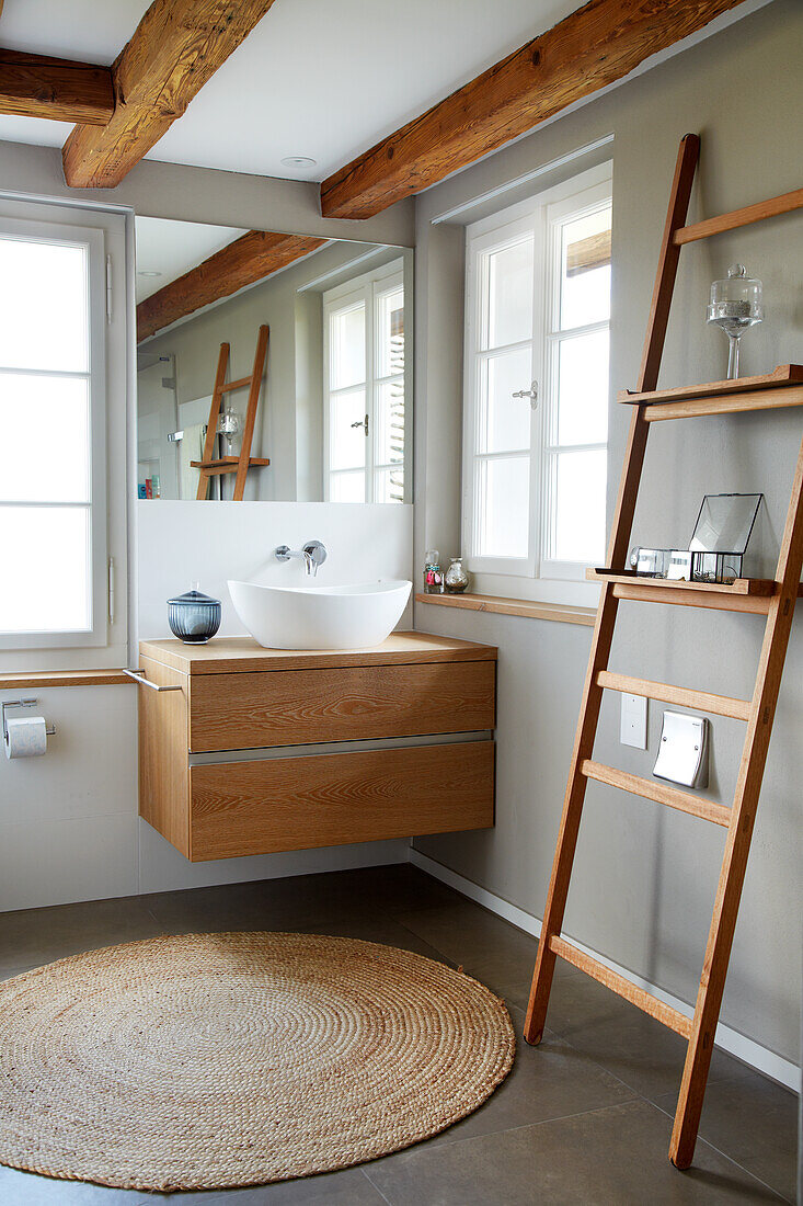 Wooden washbasin and decorative ladder in the bathroom with rattan rug