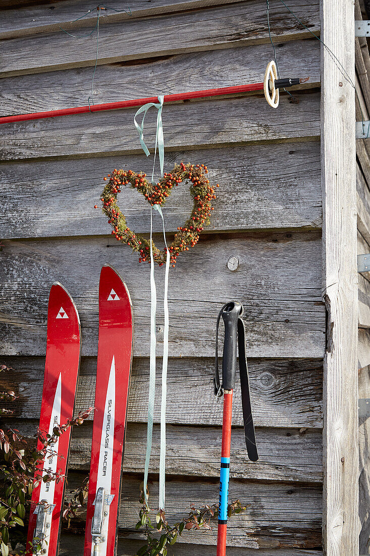 Decorative skis and heart-shaped wreath on wooden wall in outdoor area