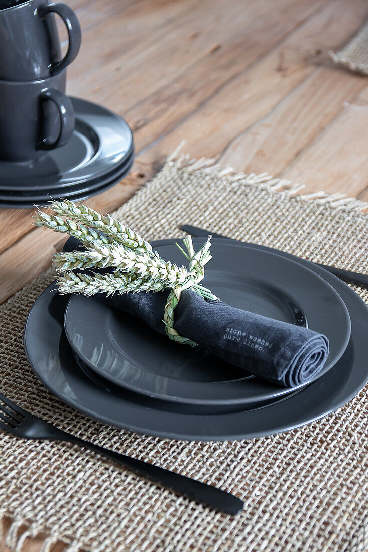 Place setting with dark grey plates and homemade wheat stalk napkin ring