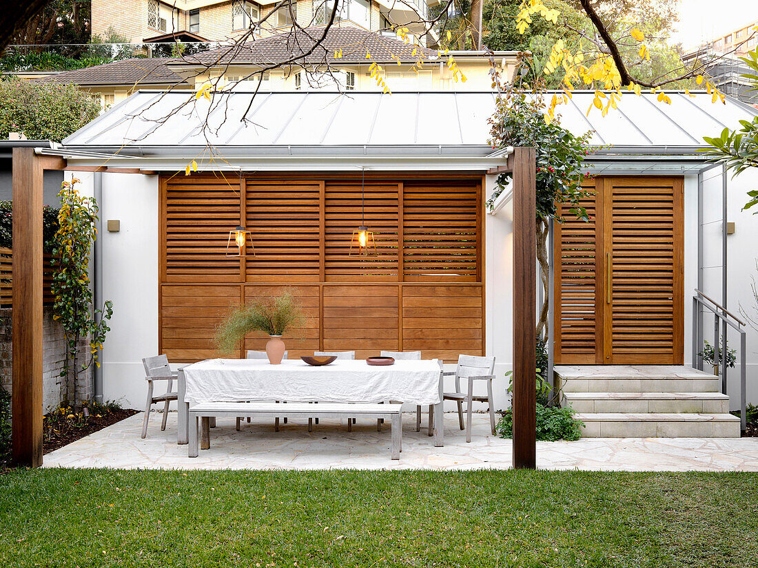 Dining table with chairs and bench on terrace in front of cedar blinds