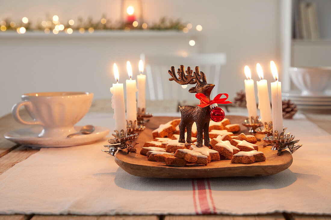 Weihnachtliche Dekoration mit Plätzchen, Rentierfigur und Kerzen auf Holztablett