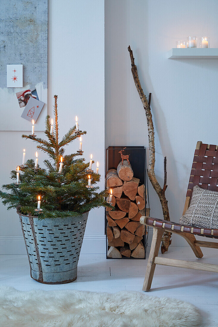 Small Christmas tree with candles in a zinc bucket, firewood and armchair