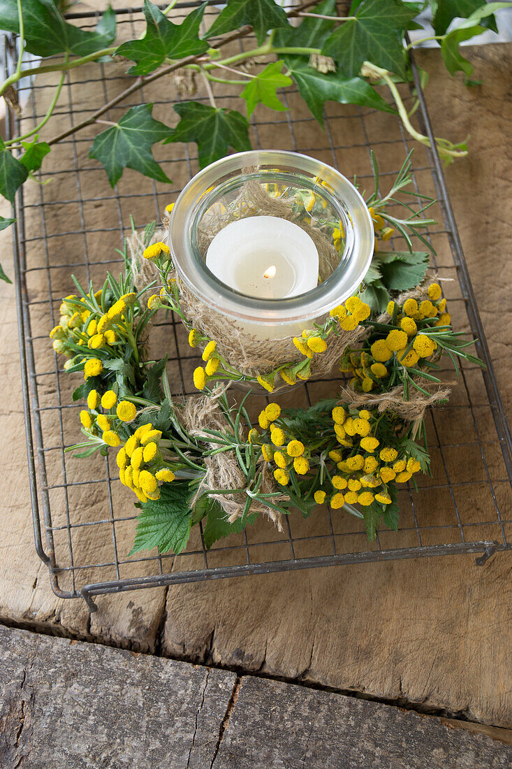 Glass jar as lantern wrapped with tansy (Tanacetum vulgare), blackberry leaves (Rubus), rosemary and sacking ribbon