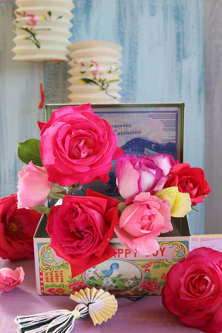 Small glass vases with roses in a vintage box, above antique paper lanterns