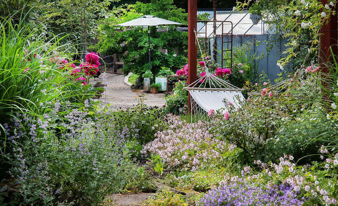 Flowering garden with hammock, sun umbrella and gravel path