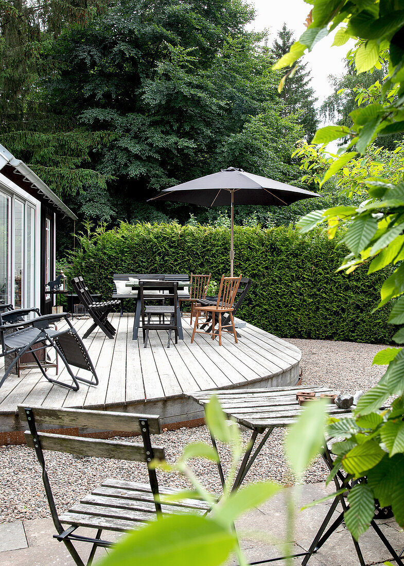 Runde Holzterrasse mit Sitzgruppe und Sonnenschirm im grünen Garten