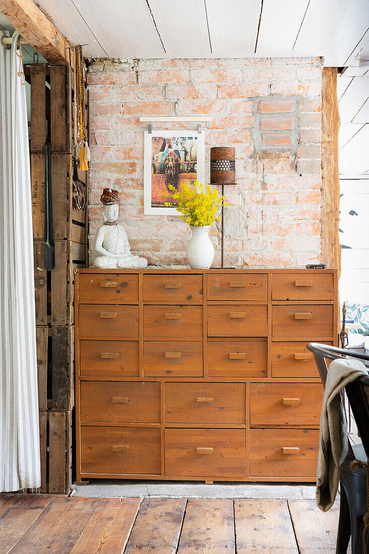 Wooden chest of drawers with lots of drawers and decorative objects, brick wall, rustic style