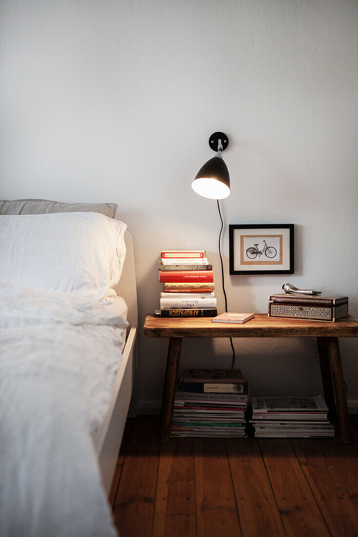 An illuminated bedside table with a stack of books next to a bed
