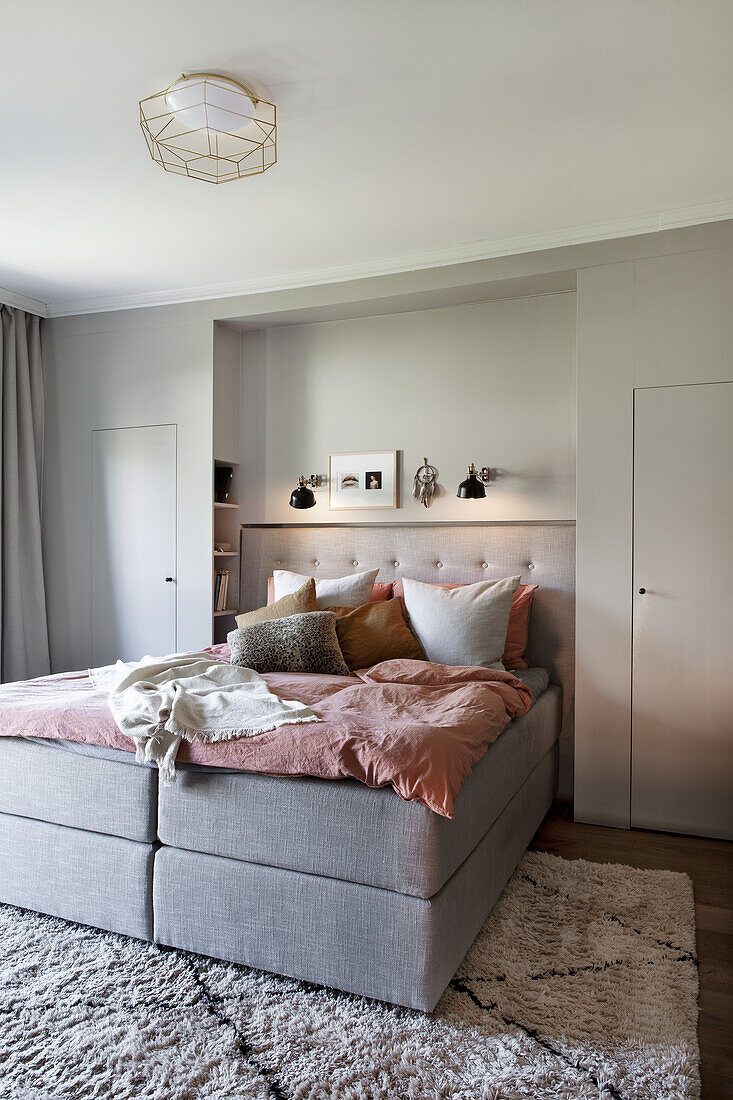 Bedroom with light grey box spring bed with pink bed linen and pillows
