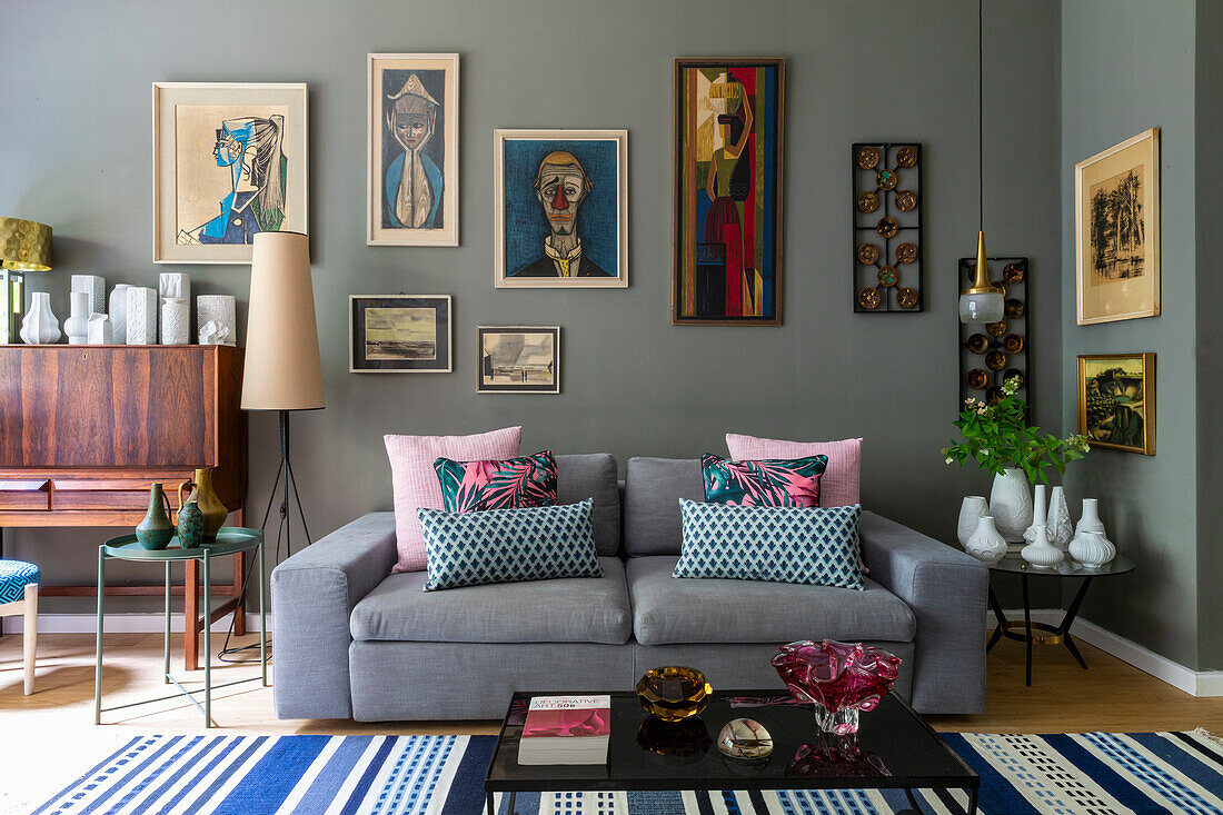 Grey upholstered sofa with throw pillows, various tables with vase collections and artwork on grey wall