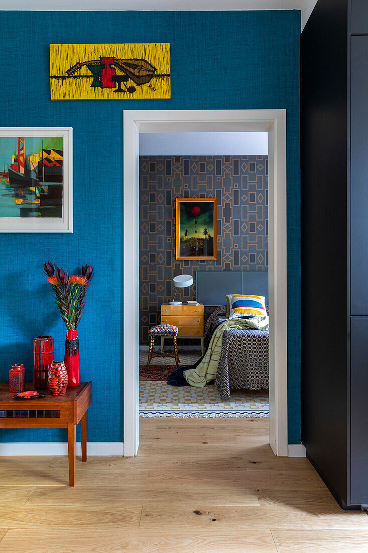 Bunte Kunstwerke an Wand mit blauer Tapete, Blick ins Schlafzimmer