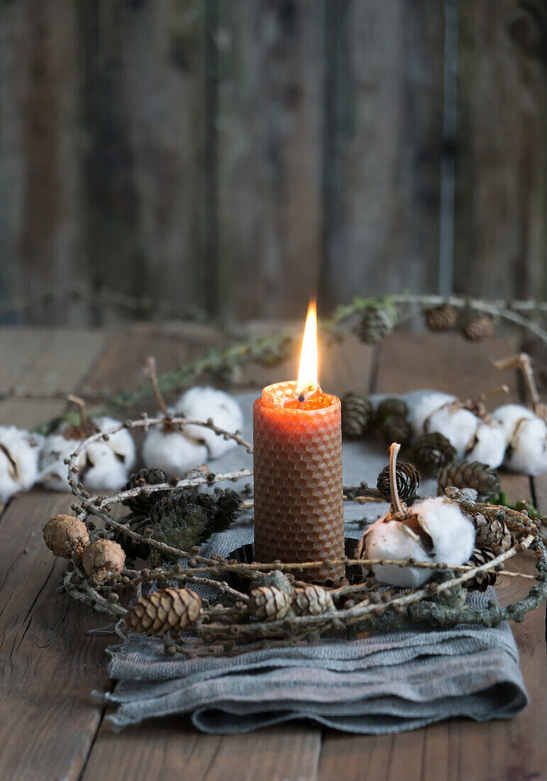 Candle made of beeswax with a wreath of larch cones and cotton on linen cloth