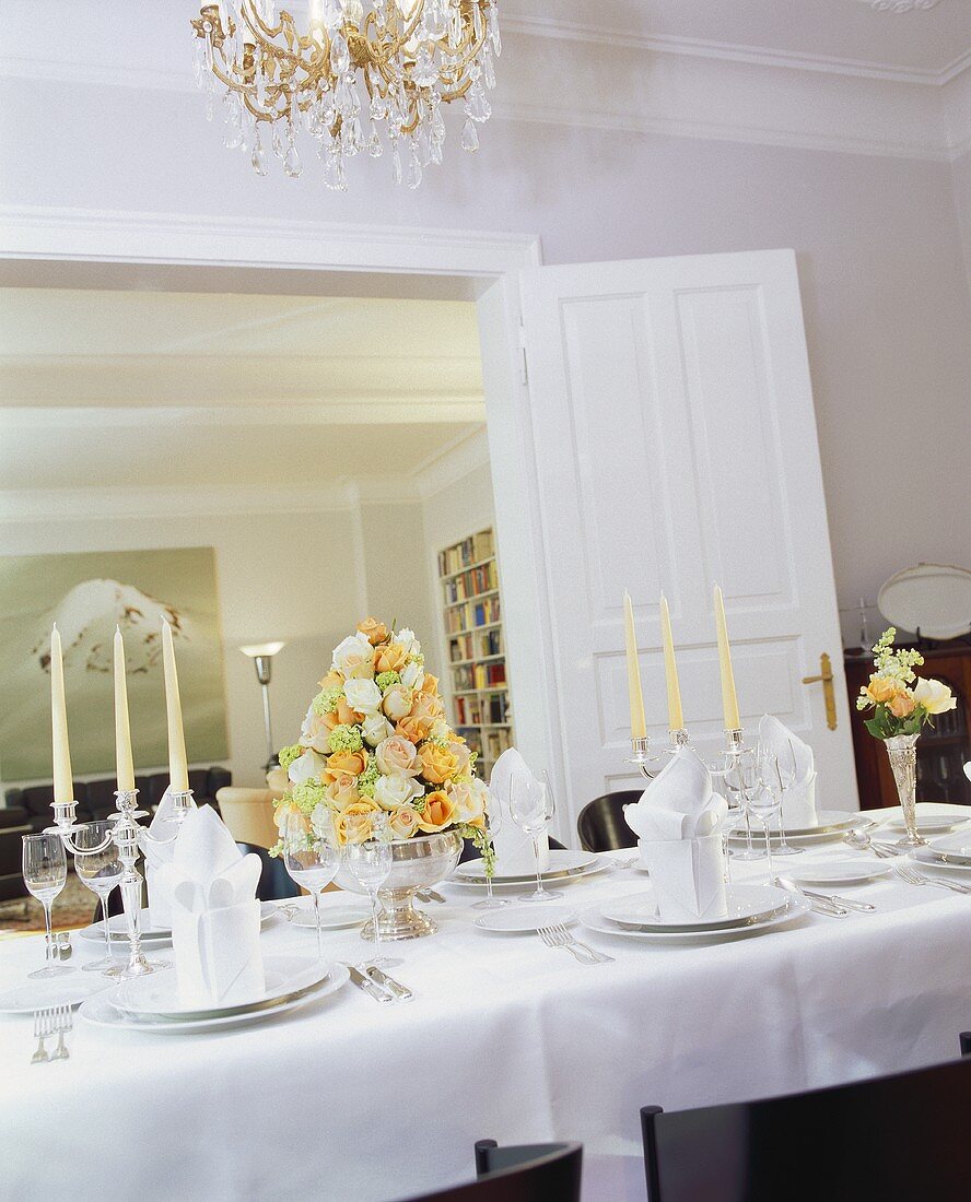 A elegant table laid in white with an arrangement of roses and silver candlesticks
