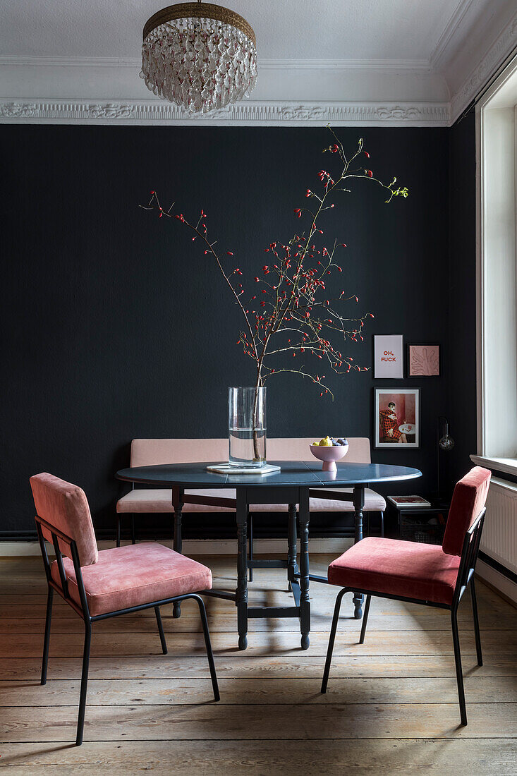 Stühle mit rosa Bezug um runden Tisch im Zimmer mit schwarzer Wand und Stuck