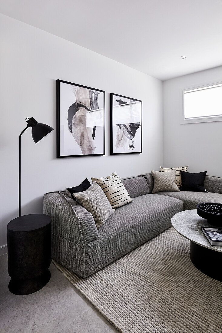 Modernes monchromes Wohnzimmer mit grauem Ecksofa, abstrakten Kunstwerken und einem Couchtisch aus Marmor