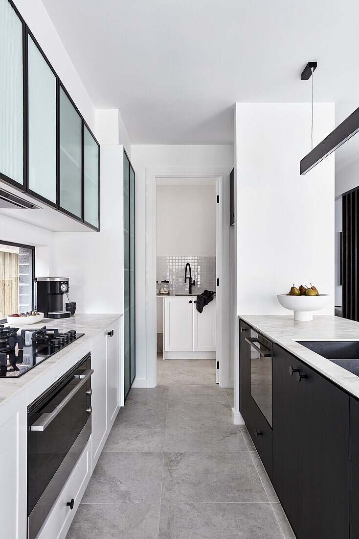 A modern monochromatic kitchen with a thin marble benchtop, black fittings and glass fronted cabinets