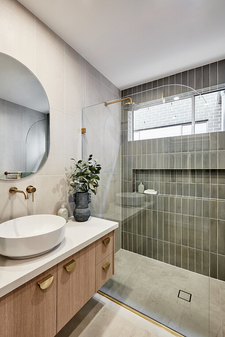 A modern Scandi-style ensuite bathroom with an olive-green tiled shower, golden fittings and an oval mirror