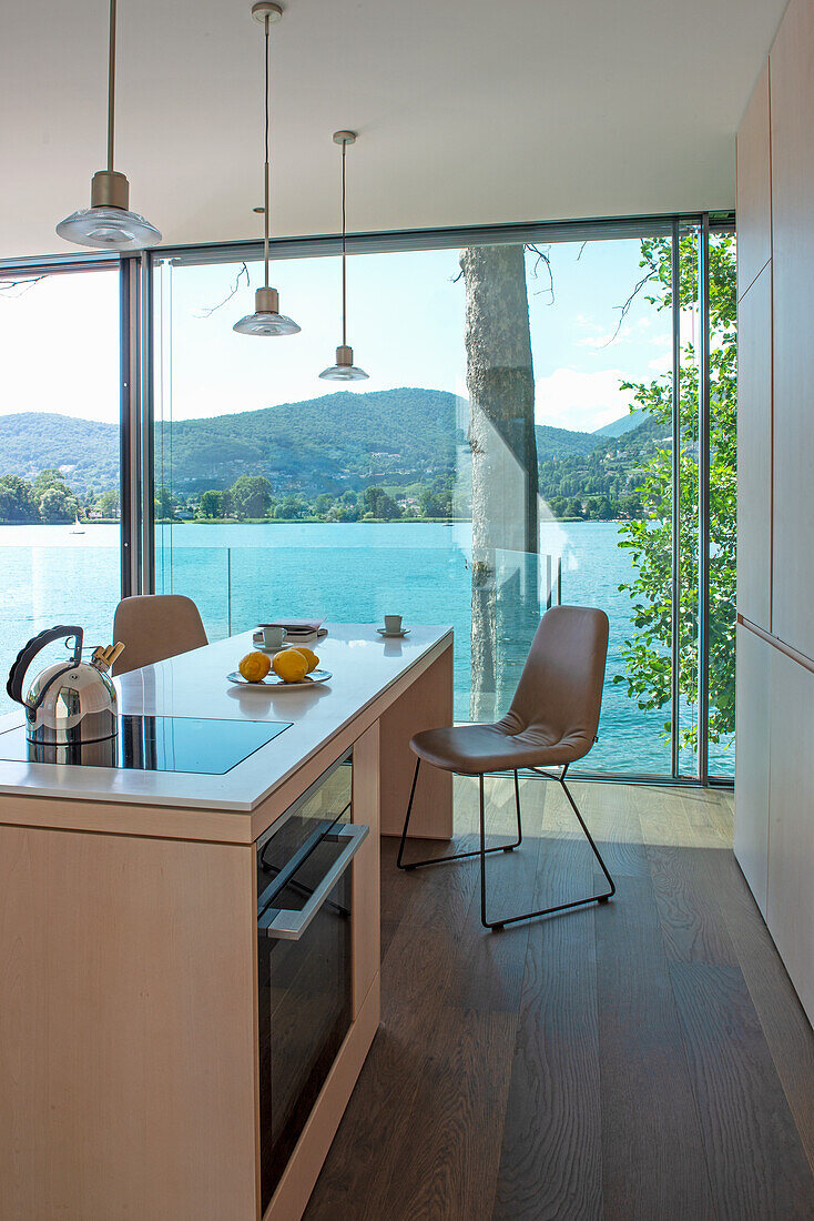 Kücheninsel mit Ess- und Kochbereich, Blick durch raumhohe Verglasung auf den See