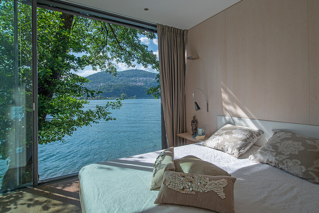 Queen sized bed in bedroom with open, floor-to-ceiling sliding door and lake view