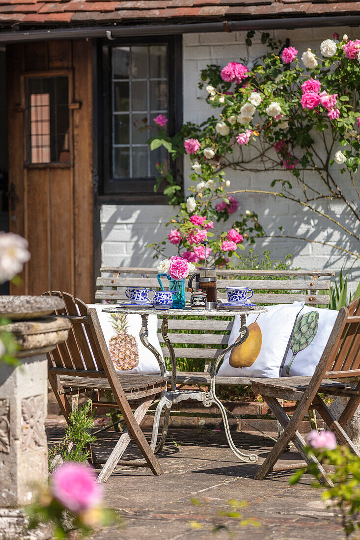 Vintage Tisch mit Stühlen auf Terrasse mit blühenden Rosen