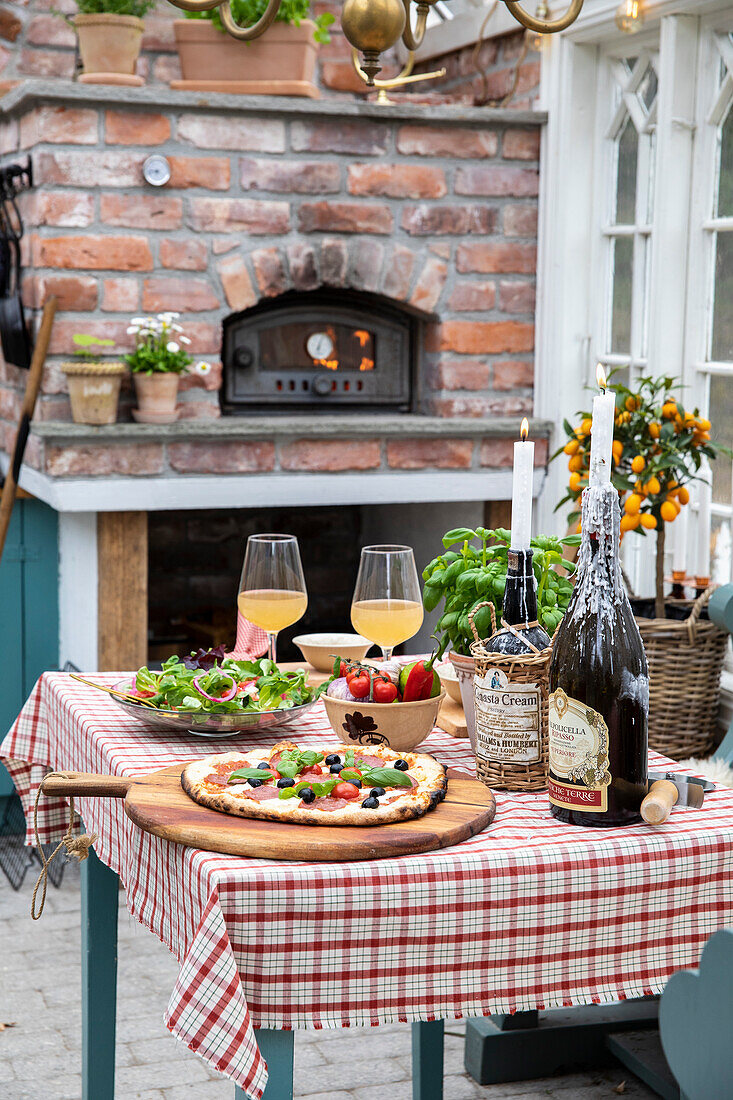 Set table with pizza on the terrace, wood-burning oven in the background