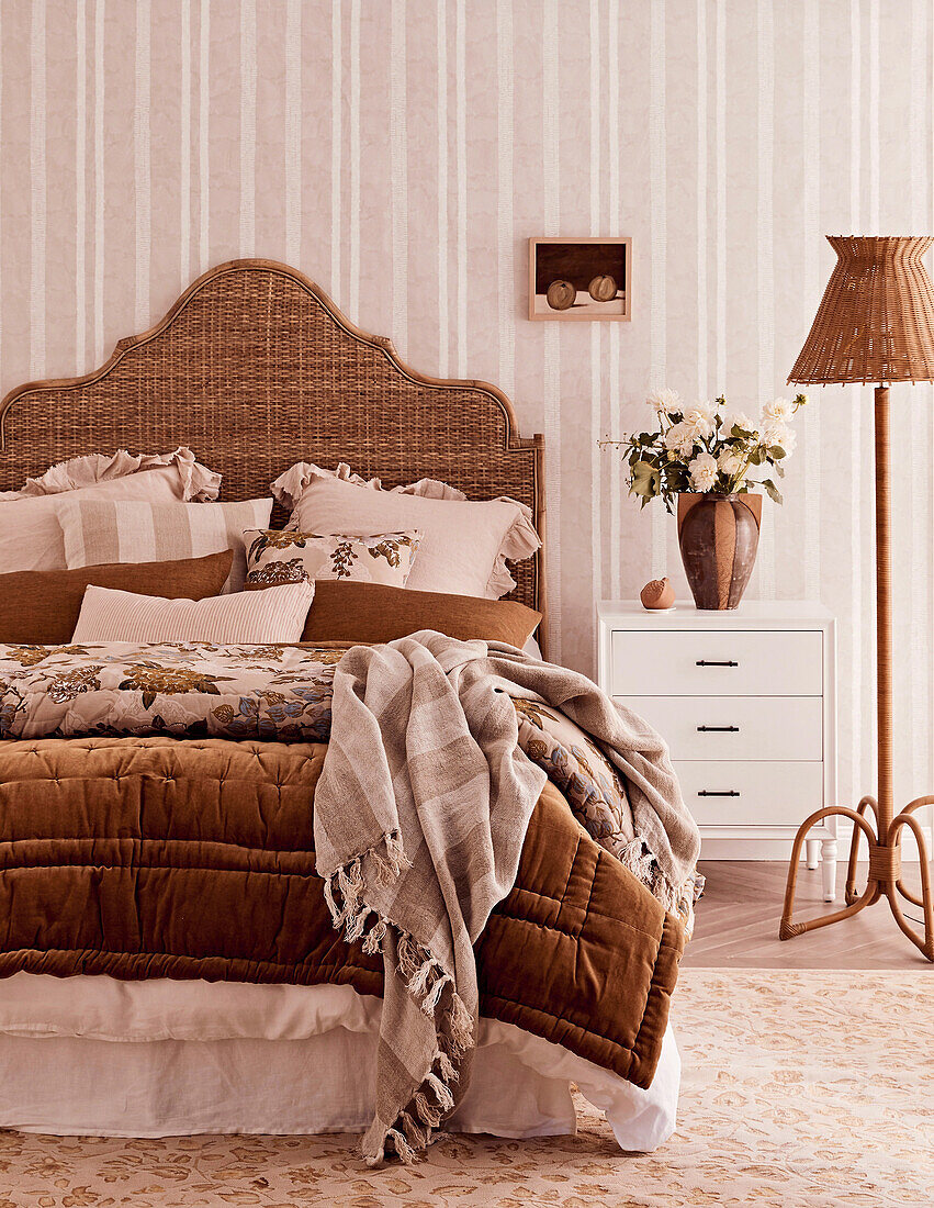 Doppelbett mit Betthaupt aus Rattan, Kissen und Decken vor gesteifter Tapete