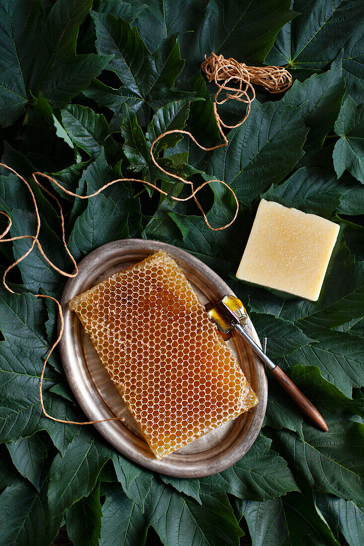 Natürliche Honigseife und Honigwabe auf Silbertablett, umgeben von Blättern