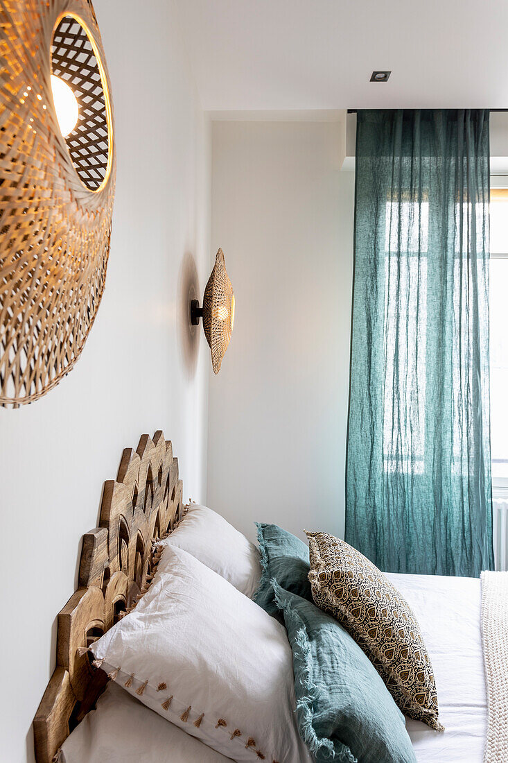 Doppelbett mit Kopfteil aus dekorativ geschnitzten Holzplatten und Wandleuchten aus Bambusgeflecht