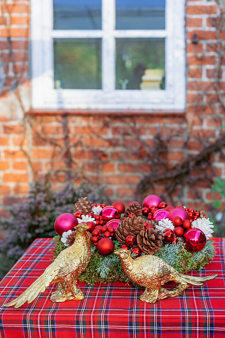 Zwei goldene Fasanen vor weihnachtlicher Kranz auf rot karierter Tischdecke