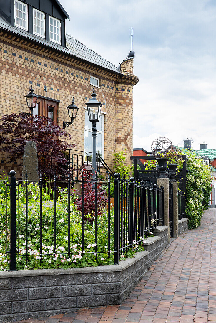 Hausfassade mit verschiedenfarbigen Ziegeln und Vorgarten mit schmiedeeisernem Zaun