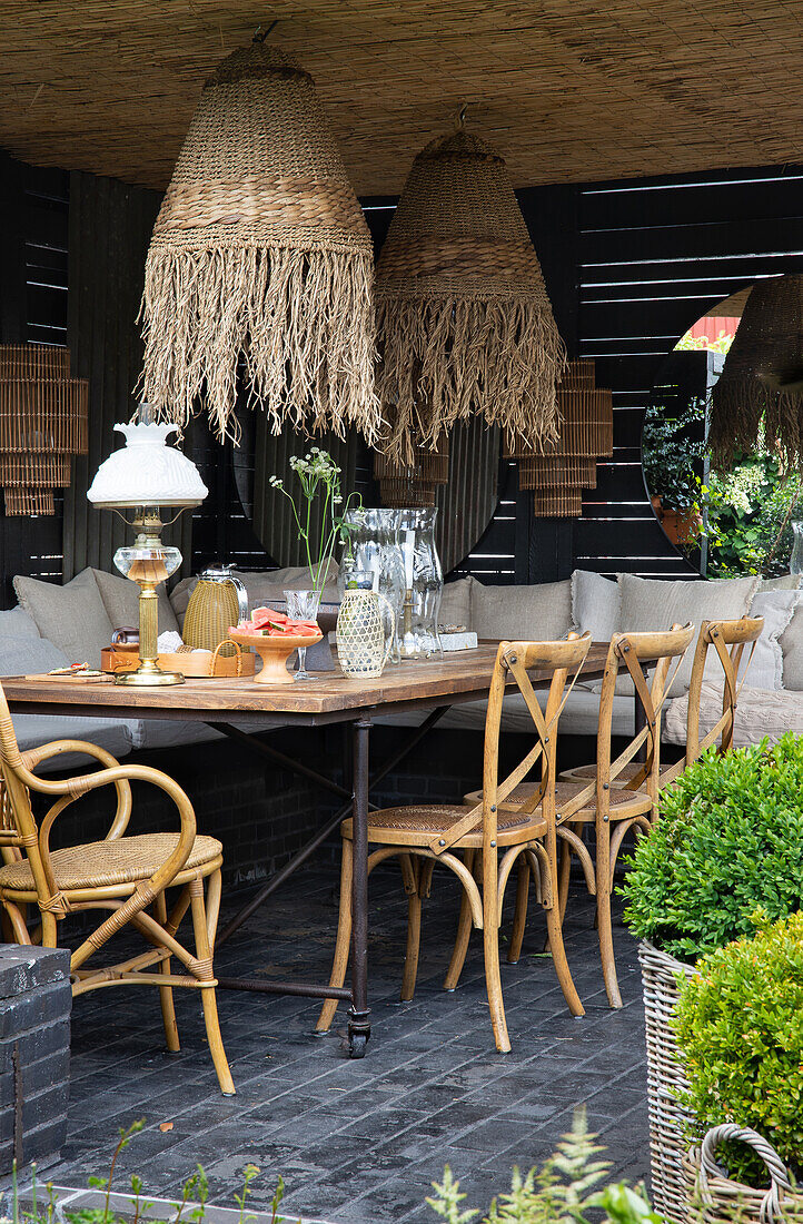Robust table with chairs and bench, sea grass lamps above on covered terrace