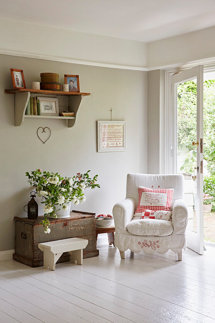 White armchair and vintage chest with cut flowers in front of patio door
