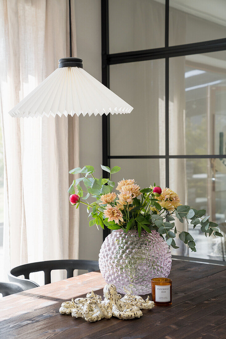 Blumenstrauß in dekorativer Vase auf Holztisch, darüber Pendelleuchte